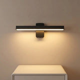 A modern linear wall sconce light fixture in a matte black finish, mounted on a beige wall above a white cabinet and illuminated with a warm glow.