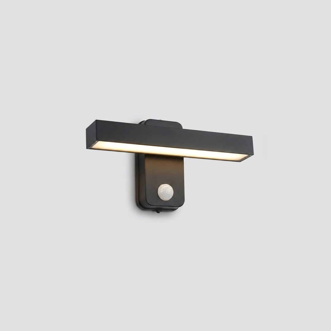 Black wall sconce with a horizontal light bar glowing warm white above a round motion sensor against a light gray background.