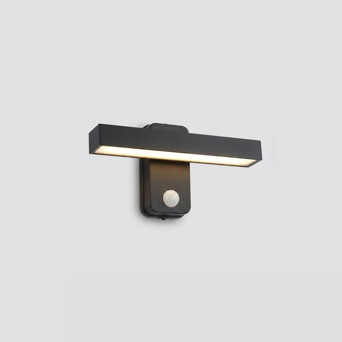 Black wall sconce with a horizontal light bar glowing warm white above a round motion sensor against a light gray background.