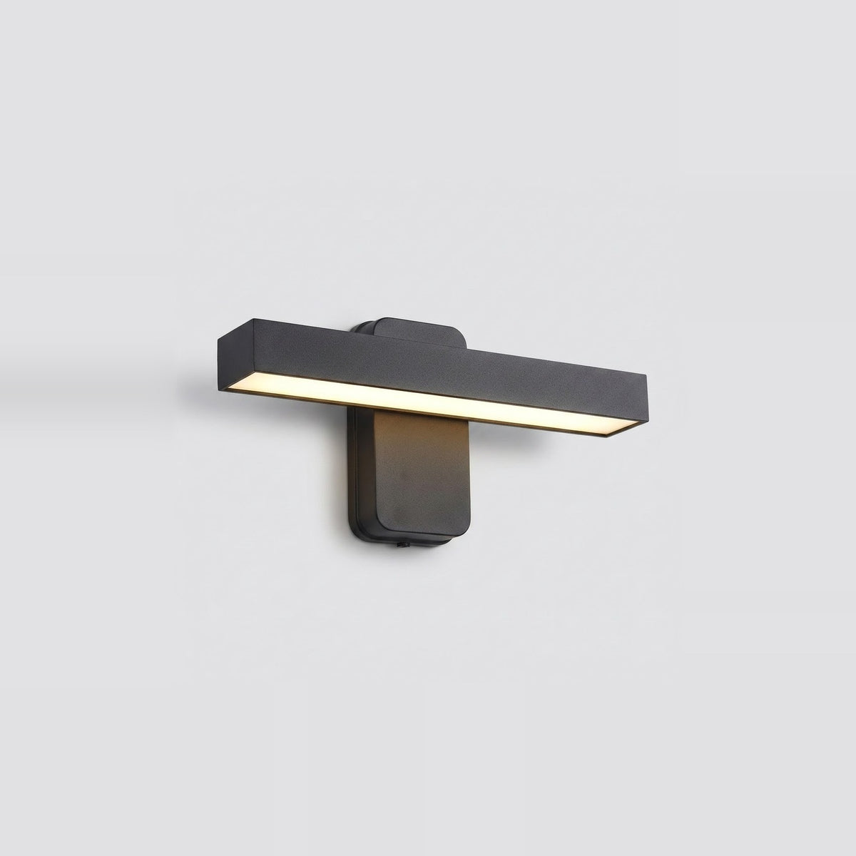 A modern matte black rectangular wall sconce with a horizontal light bar, shown mounted on a light gray wall and illuminated.
