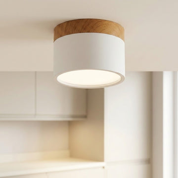 White cylindrical LED downlight with wood trim, illuminated on a ceiling above pale kitchen cabinets.