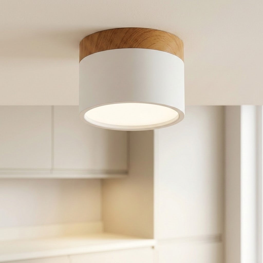 White cylindrical LED downlight with wood trim, illuminated on a ceiling above pale kitchen cabinets.