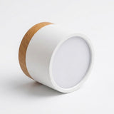 White cylindrical LED downlight with wood trim rests on its side against a white background, showing its circular diffuser.