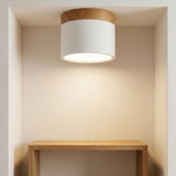 A white cylindrical LED downlight with wood trim illuminates a cream alcove above a wooden shelf.