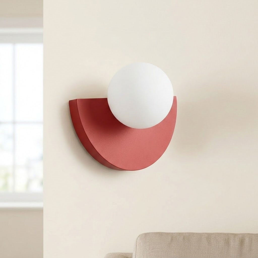 Terracotta-red wall sconce with a white globe shade, viewed at an angle on a cream wall above a beige sofa.