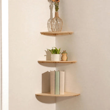 Three light natural pine corner shelves in a cream corner holding a flower vase, a potted plant and frog ornament, and three upright books.