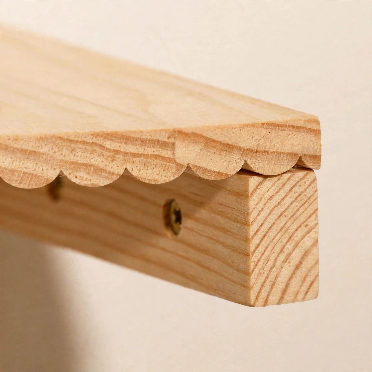 Close-up of a light natural pine corner shelf showing its scalloped front edge, continuous wood grain, and wooden mounting cleat with a visible screw underneath.