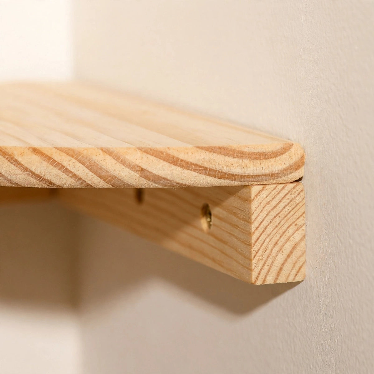 Close-up side view of a light natural pine corner shelf end against a cream wall, showing rounded edge grain and wooden cleat with a screw.