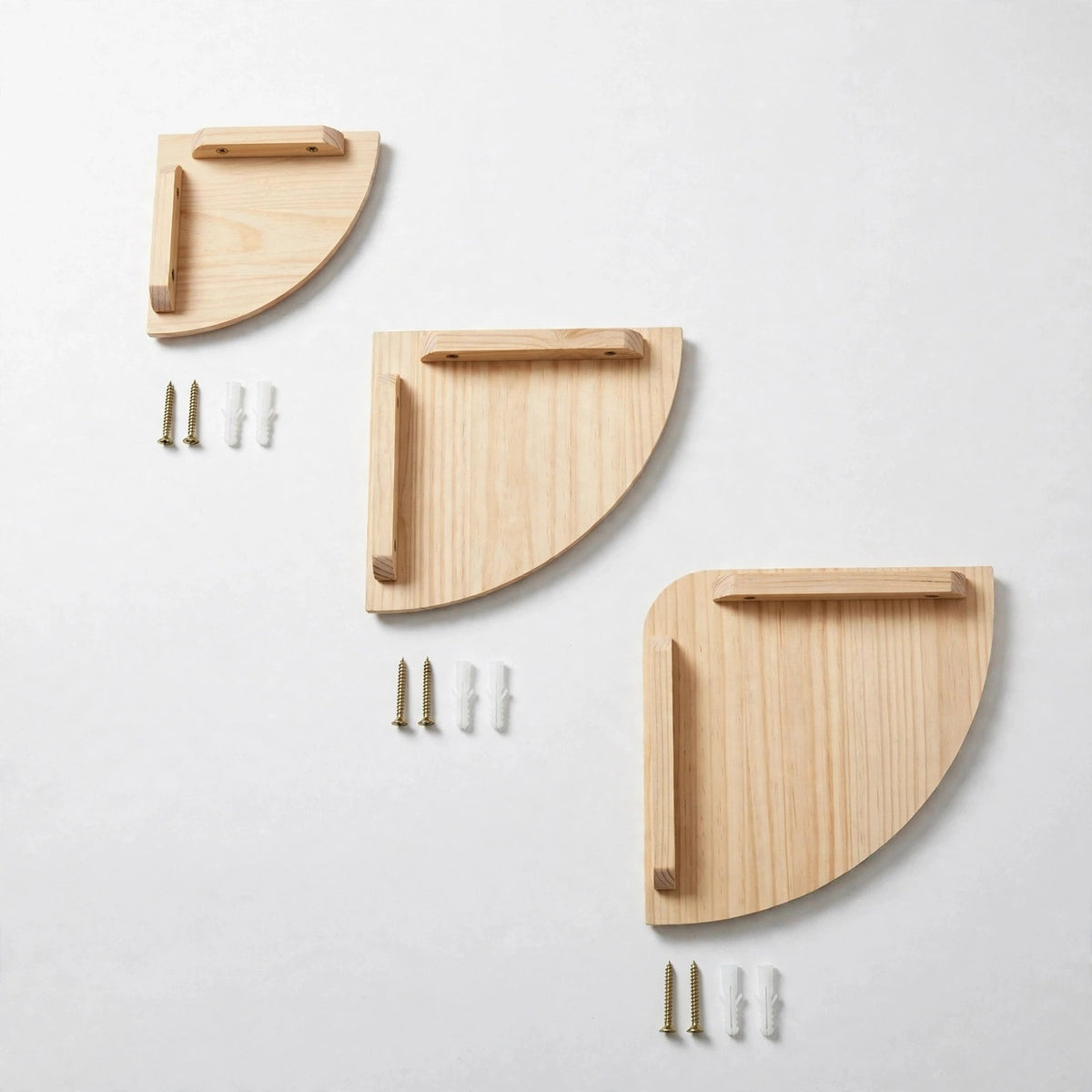 Three light natural pine quarter-round corner shelves in small, medium and large sizes on a white background, each beside gold screws and white plugs.