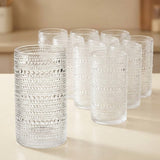 A set of clear textured glass tumblers with a raised bubble pattern, arranged on a light beige tabletop in a softly blurred indoor setting.