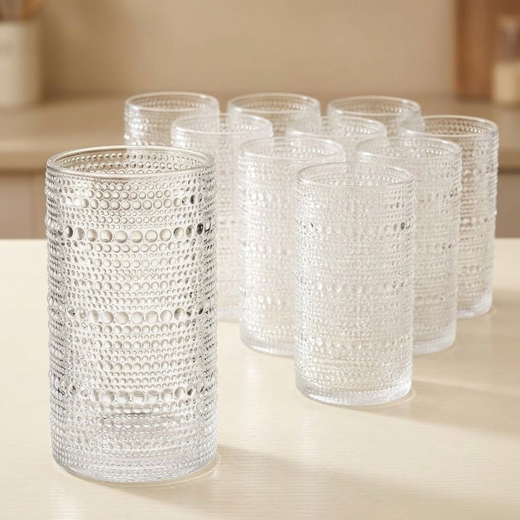 A set of clear textured glass tumblers with a raised bubble pattern, arranged on a light beige tabletop in a softly blurred indoor setting.