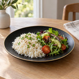 Black gold rim ceramic dinner plate serves rice and salad at a softly lit home dining table.