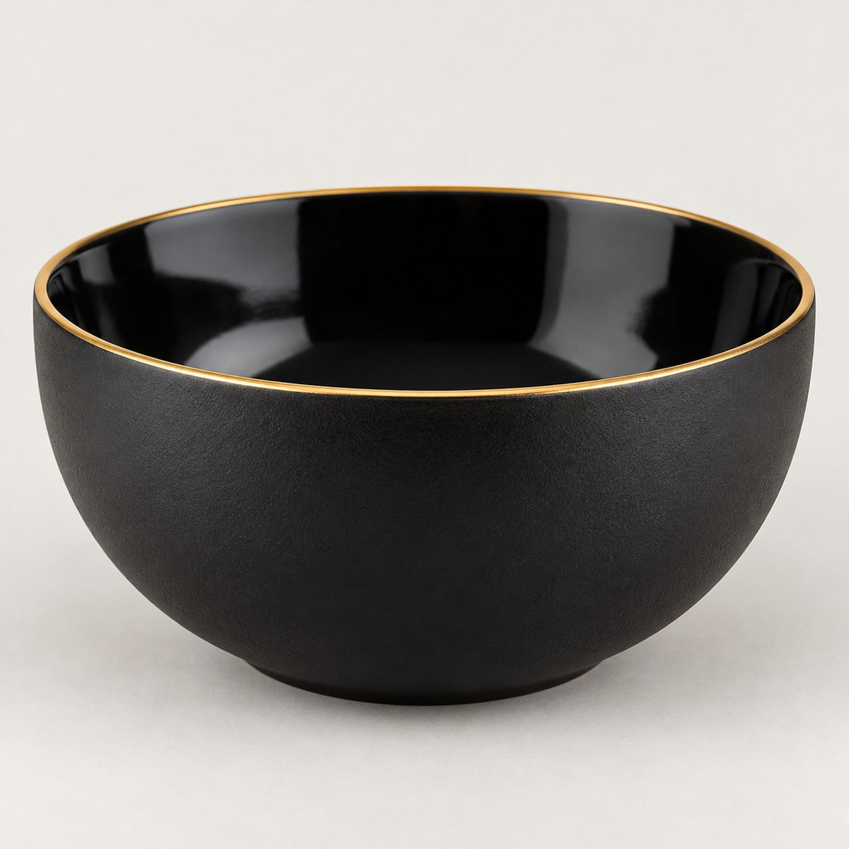 Single deep black ceramic bowl with a gold rim shown from the side on a light studio background.