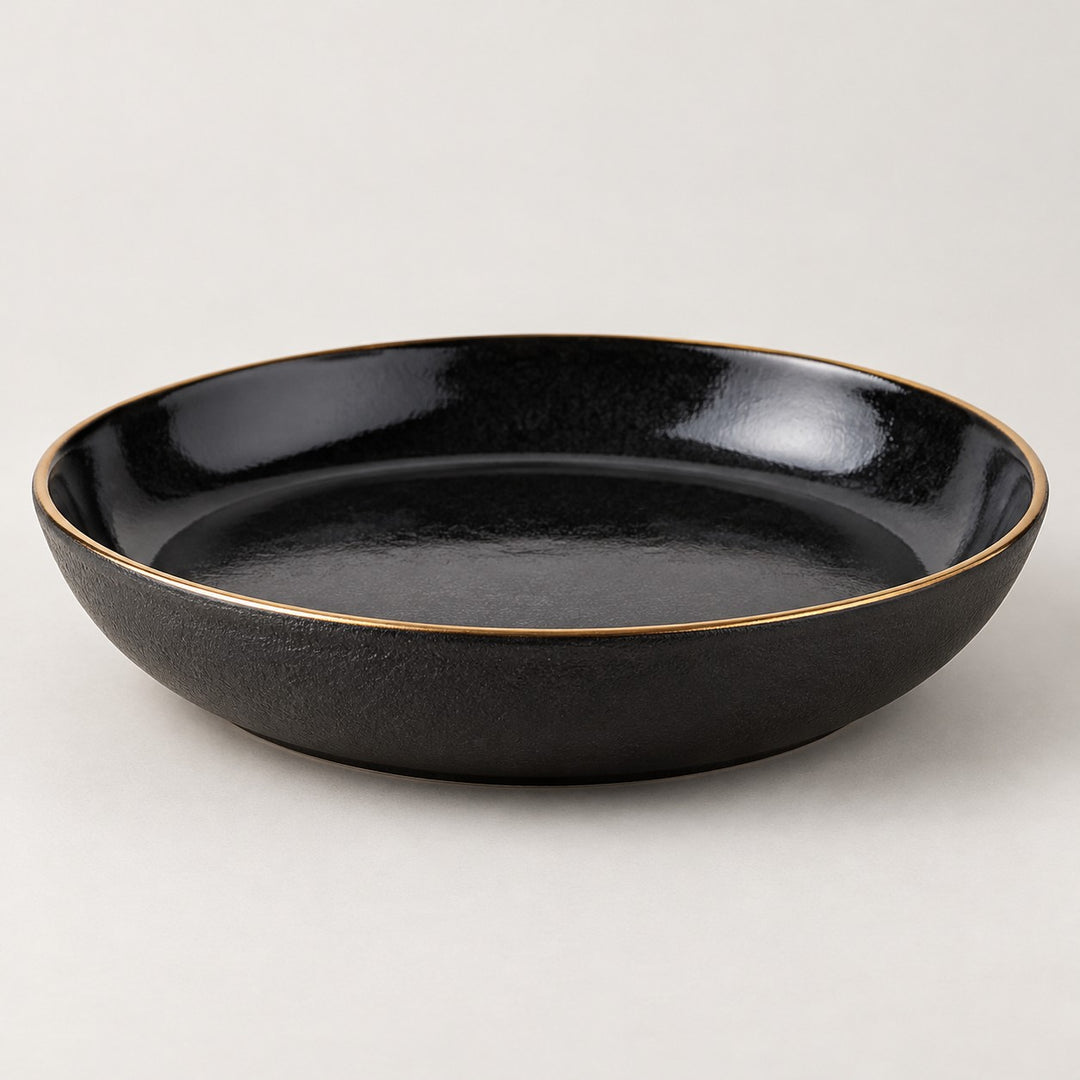 Single shallow black ceramic deep plate with a gold rim on a light studio background.