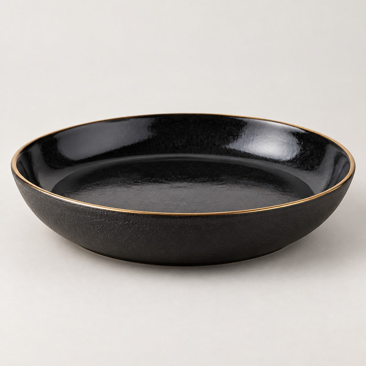 Single shallow black ceramic deep plate with a gold rim on a light studio background.