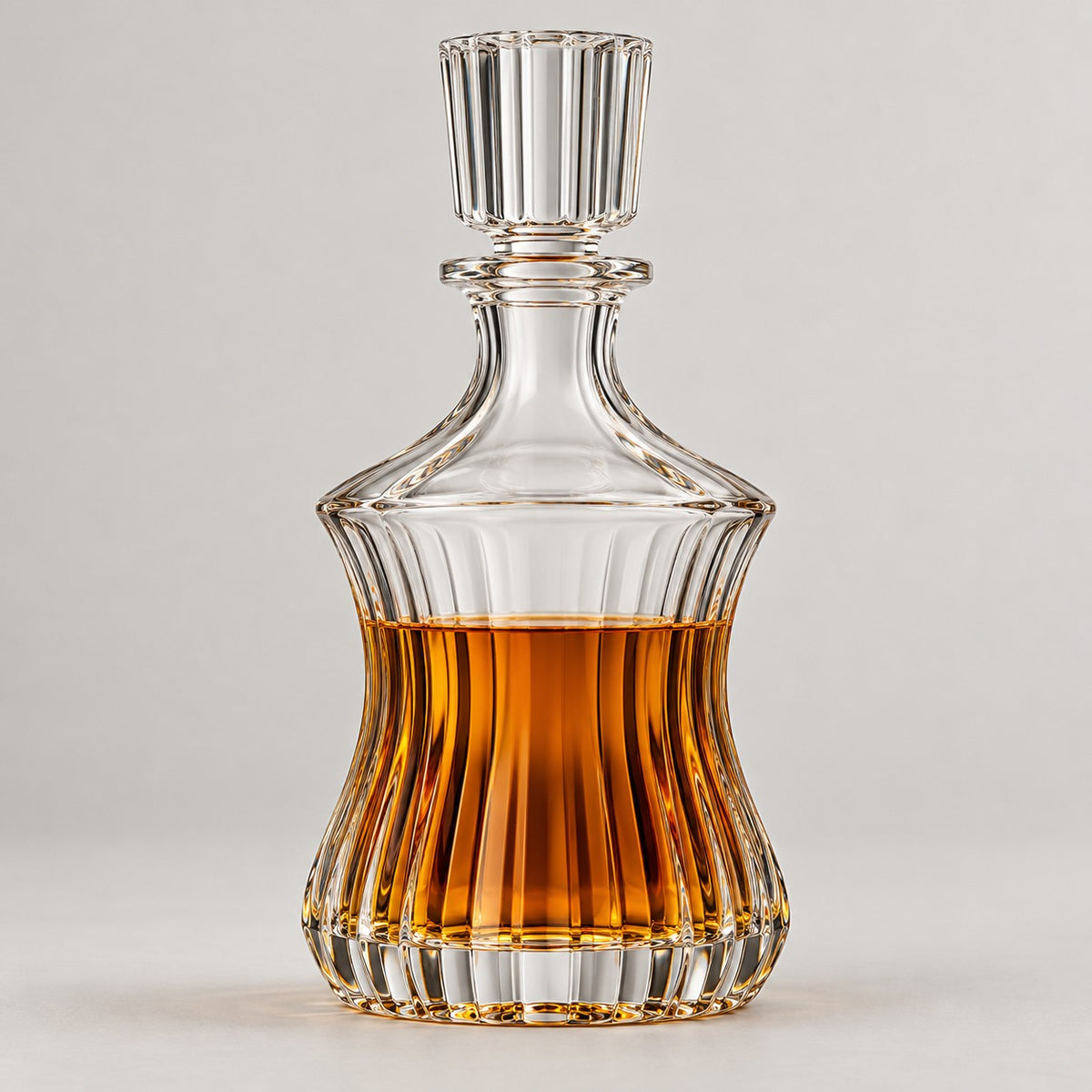 Fluted Hourglass glass wine decanter with amber drink on a pale studio backdrop.