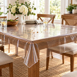 Clear disposable plastic tablecloth covers a dining table with crumbs and a small spill during home use.
