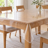 Clear disposable plastic tablecloth drapes over a light oak table while leaving the wood grain visible.