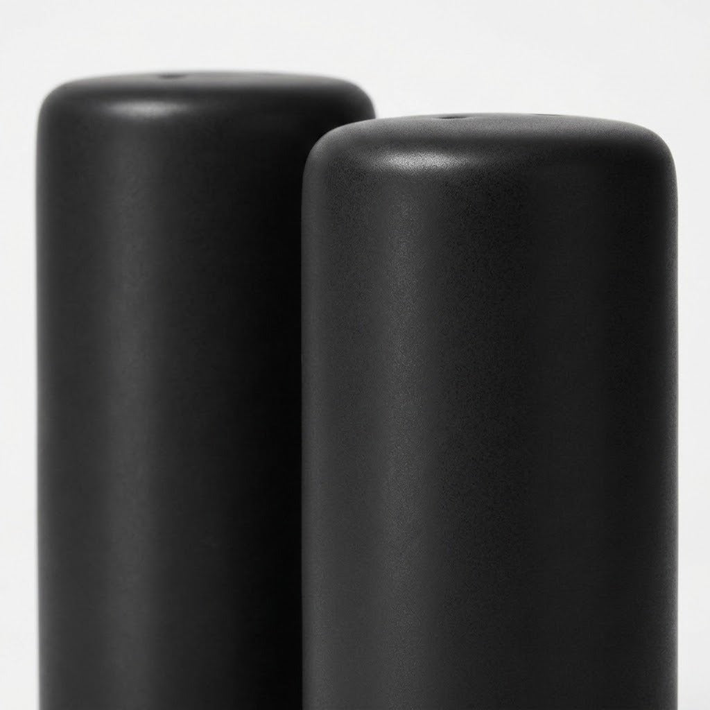 Two matte black cylindrical objects, likely candle holders or decorative vases, shown close-up against a light gray background.
