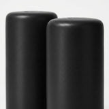 Two matte black cylindrical objects, likely candle holders or decorative vases, shown close-up against a light gray background.
