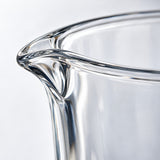 Macro view of the measuring cup's thick clear glass rim and smooth polished spout.