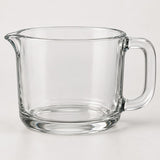 The clear glass 2-cup measuring cup stands alone against a pale neutral studio backdrop.