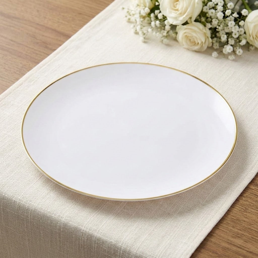A round white plate with a thin gold rim, placed on a beige table runner with white roses in the background.