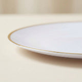 A close-up of a white ceramic plate with a delicate gold rim, resting on a neutral beige surface.