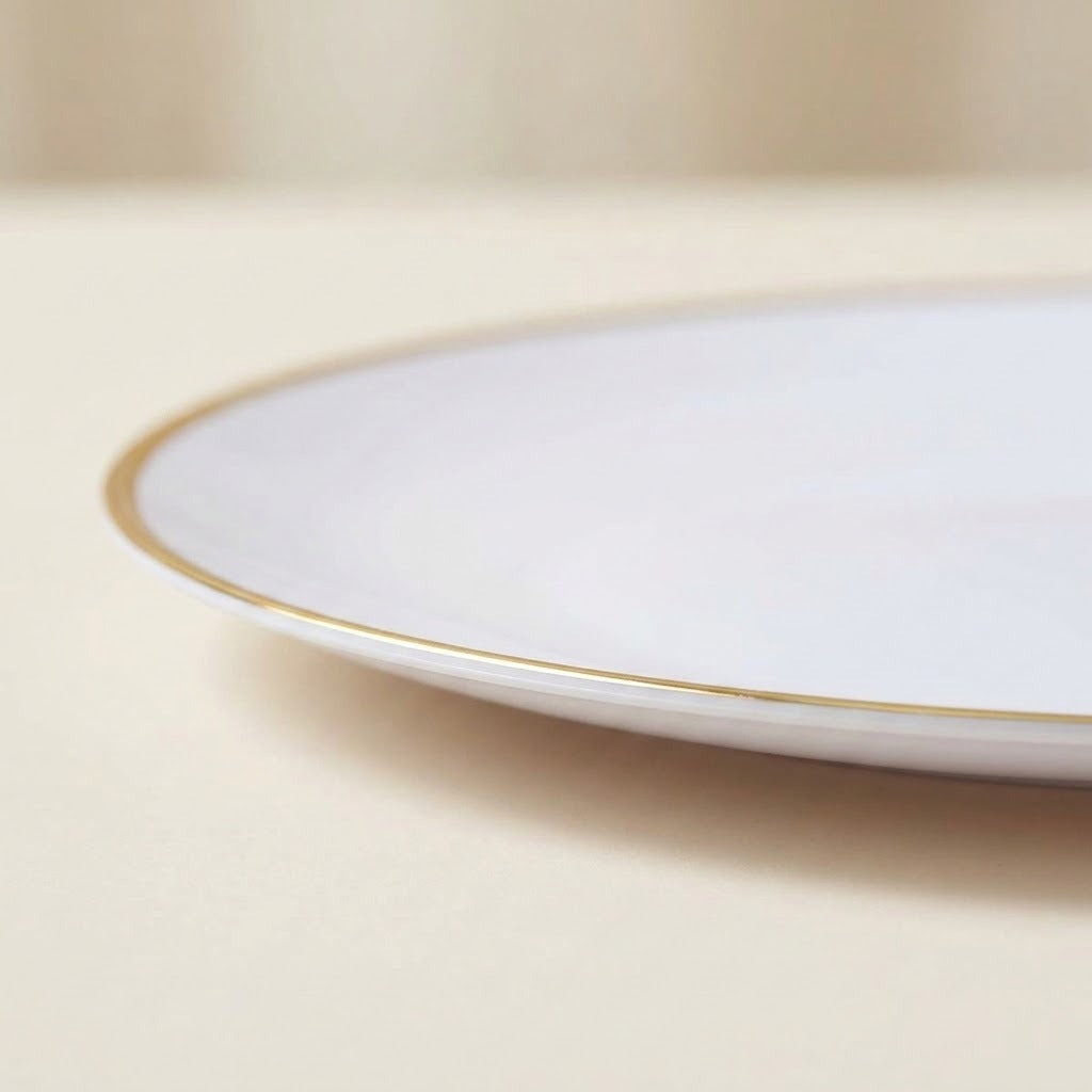 A close-up of a white ceramic plate with a delicate gold rim, resting on a neutral beige surface.
