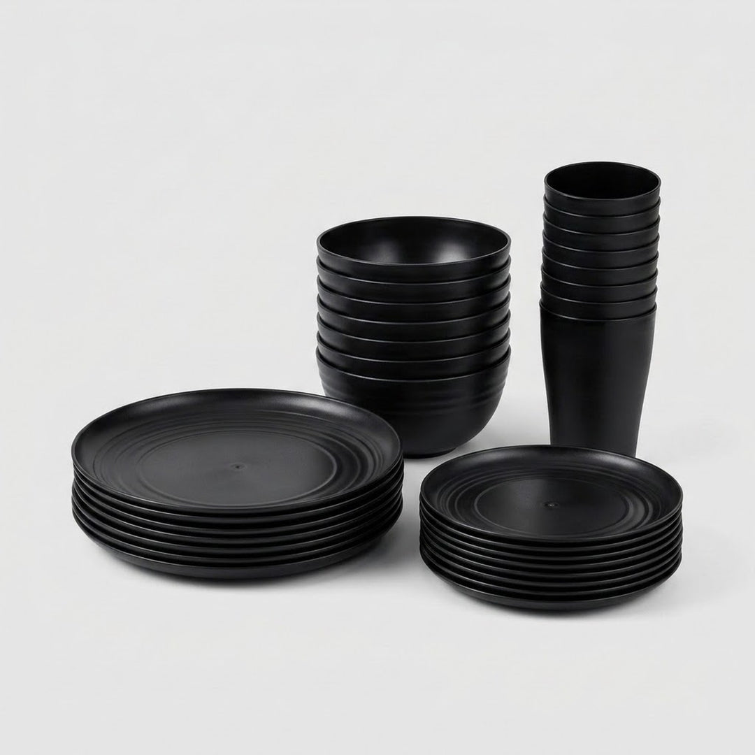 A set of matte black dinnerware, including plates, bowls, and cups, neatly stacked in three groups on a light gray background.
