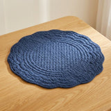 A round quilted blue placemat with scalloped edges resting on a light wood table.