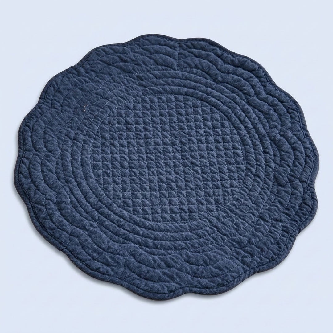 A round quilted baby play mat with a scalloped edge, featuring concentric diamond-quilted patterns in a dark navy blue color, shown on a light blue background.