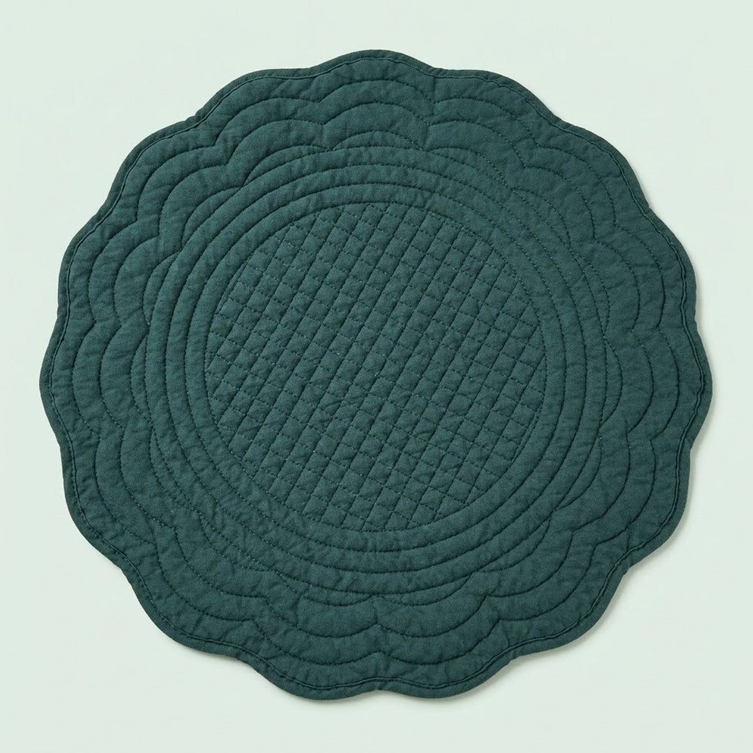 A round quilted placemat with a scalloped edge in a dark teal green color, shown flat against a light mint green background.