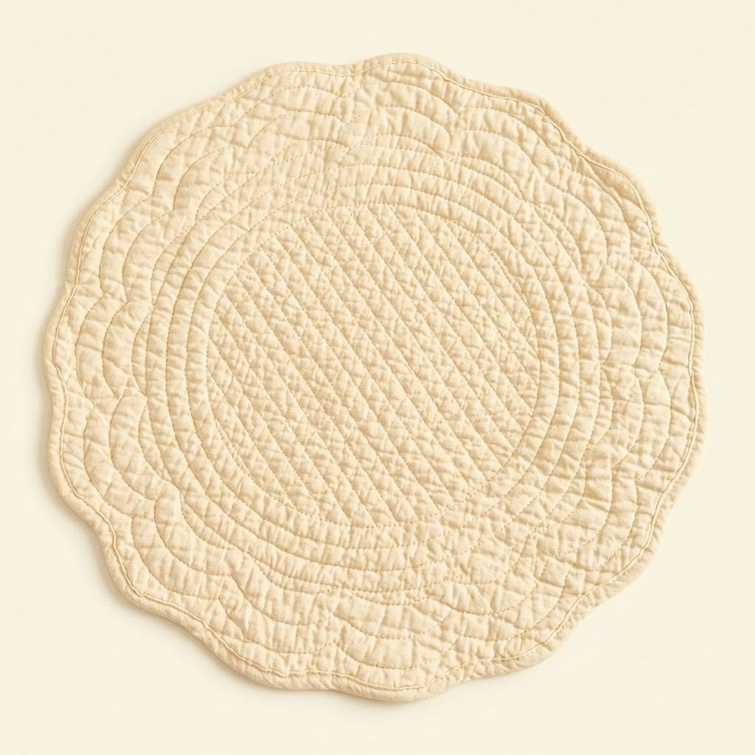 A round quilted placemat with a scalloped edge in a light cream or beige color, shown flat against a matching light beige background.