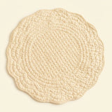 A round quilted placemat with a scalloped edge in a light cream or beige color, shown flat against a matching light beige background.