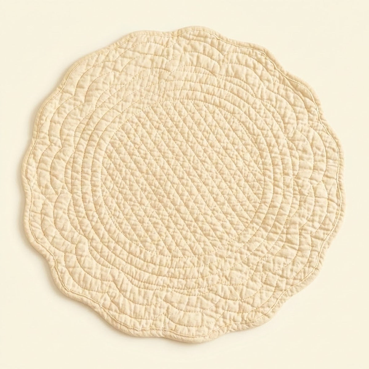 A round quilted placemat with a scalloped edge in a light cream or beige color, shown flat against a matching light beige background.