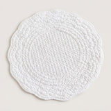 A round white quilted placemat with a scalloped edge, shown flat against a light beige background.