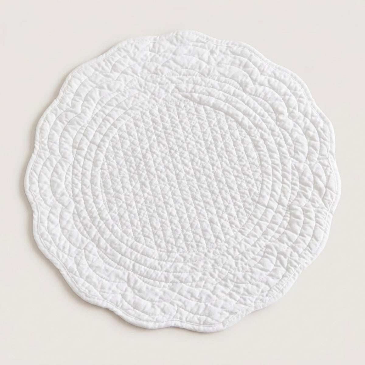 A round white quilted placemat with a scalloped edge, shown flat against a light beige background.