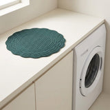 A round teal green quilted laundry mat with a scalloped edge sits on a cream-colored countertop next to a white washing machine.