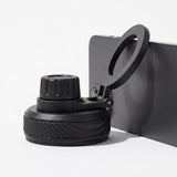 A black phone mount accessory with a circular clip and textured base, shown attached to the side of a dark smartphone on a clean white background.
