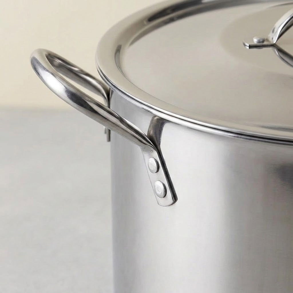 Close-up of a stainless steel stockpot with a matching lid, showing the shiny metal surface and side handle attachment on a light neutral background.