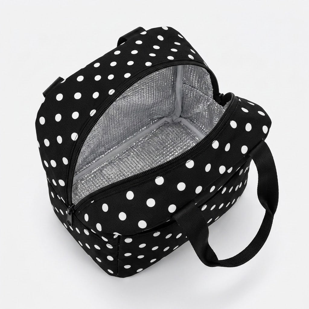 A black and white polka dot lunch bag with an open zipper revealing a silver insulated interior, shown on a light gray background.