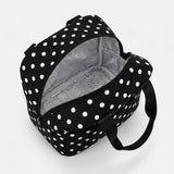 A black and white polka dot lunch bag with an open zipper revealing a silver insulated interior, shown on a light gray background.