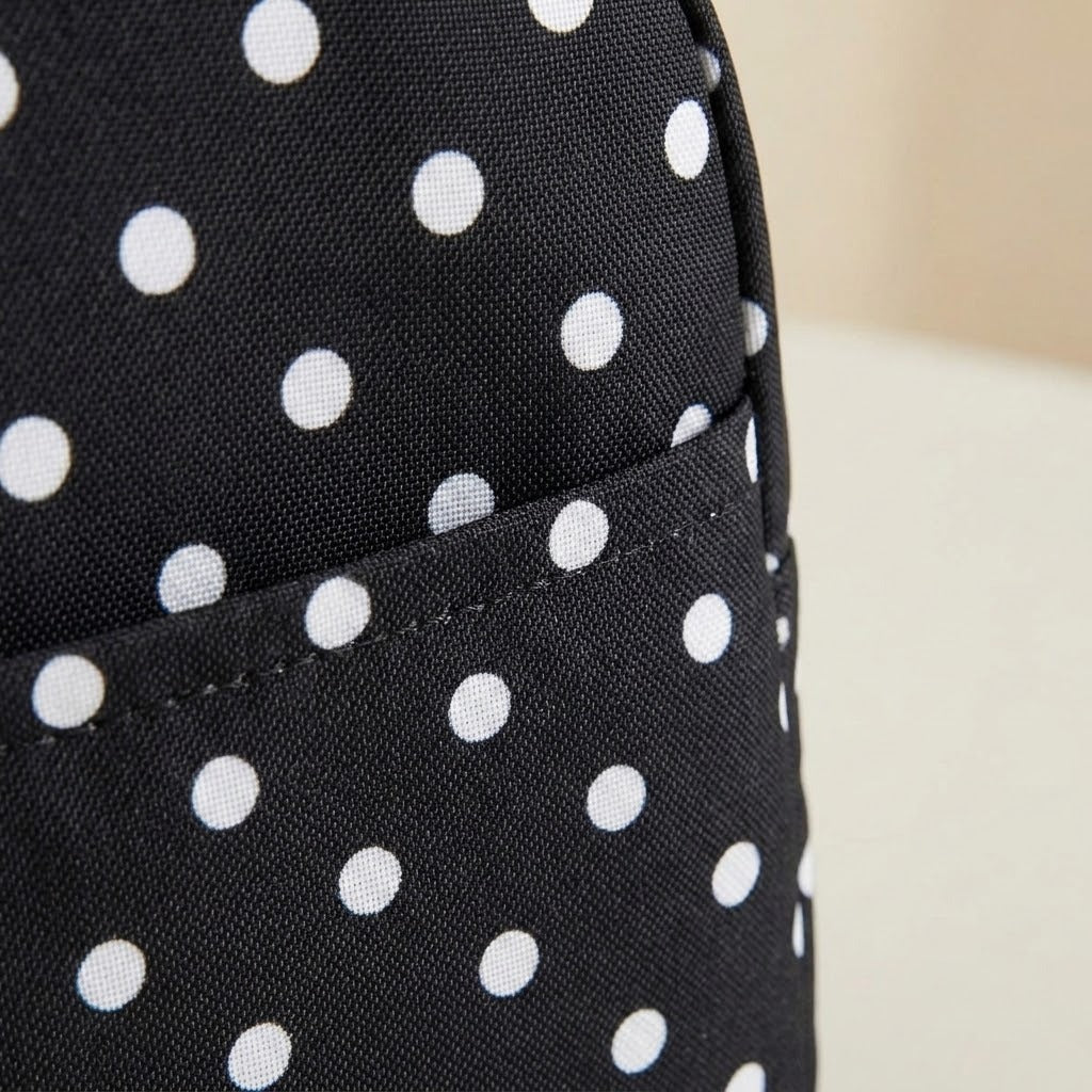 Close-up of a black fabric item with a white polka dot pattern and a stitched pocket, photographed against a light neutral background.