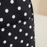 Close-up of a black fabric item with a white polka dot pattern and a stitched pocket, photographed against a light neutral background.