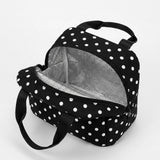 A black and white polka dot lunch bag with a silver insulated interior, shown open on a light gray background.