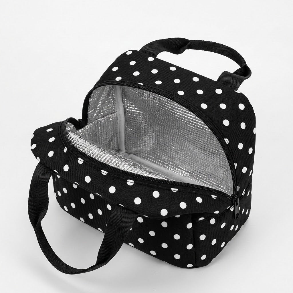 A black and white polka dot lunch bag with a silver insulated interior, shown open on a light gray background.