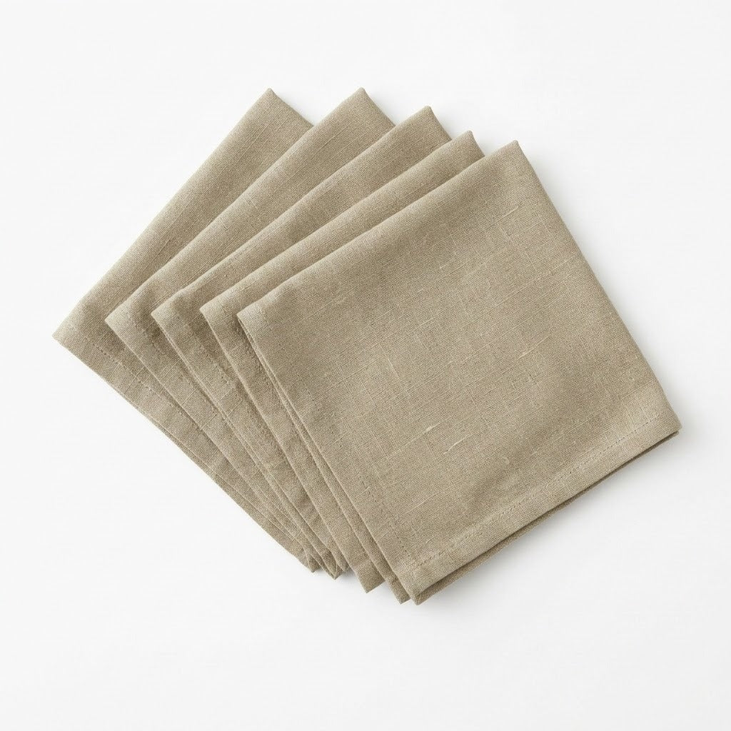 Four folded square linen napkins in a light taupe-beige color, arranged in a fan shape on a clean white background.