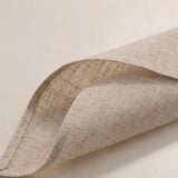 A close-up of a folded beige linen fabric napkin or cloth, showing its natural woven texture against a plain light background.