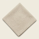 A folded beige linen napkin with a visible woven texture and stitched border, displayed on a solid cream background.